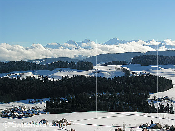 Foto: Winterlandschaft Emmental mit Weiler, Wäldern, Hügelzügen und Eiger, Mönch, Jungfrau mit Wolken.