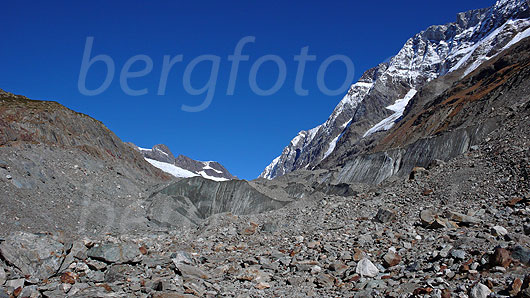 Foto: Gletschervorfeld am Langgletscher mit viel Geröll und mit Schutt bedeckten Eismassen. Darüber Grasbänder in den Herbstfarben und leicht überzuckerte Felsen der umliegenden Berge. Zu sehen sind Lötschenlücke, Sattelhorn, Distlighorn und Schinhorn.