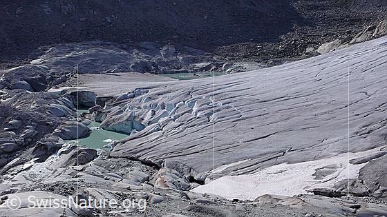 Foto: Ursprung der Rhone. Gletscherzunge und Gletschertor des Rhonegletschers mit Gletscherabbruch in einen neu entstandenen Gletschersee. Der Gletscher hat auf seinem Rückzug einen Felsriegel freigelegt an welchem sich das Wasser nun staut. Durch weiteres Abschmelzen des Gletschers wird sich der See vergrössern und könnte im Laufe der Zeit eine Naturgefahr darstellen.
