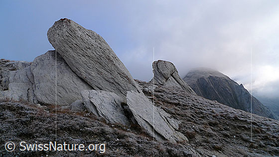 Foto: Felsblöcke in urtümlicher Landschaft. 
Interessante Formen geschichteter Felsblöcke in kalter Raureiflandschaft mit Restbewölkung über den Bergen.