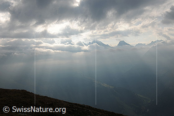 Foto: Lichtstimmung im Gebirge. Sonnenstrahlen brechen durch die Restwolken über einer Bergkette.