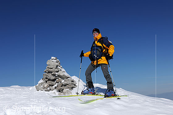 Foto: Skitourenfahrerin neben Steinmann auf dem Gipfel.