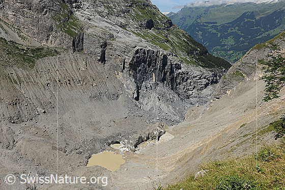 Foto: Gletschersee und Bergsturzgebiet oberhalb Grindelwald. Die braune Farbe des Wassers stammt von Erdreich, welches durch Murgänge (rechts im Bild) in den See gelangte. Am Talausgang ist das Felssturzgebiet (Schlossplatte) zu sehen.
