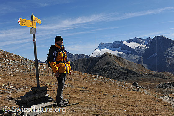 Foto: Wanderer bei Wegweiser. Wanderin geniesst die Aussicht. Im Hintergrund ist der Monte Leone zu sehen.