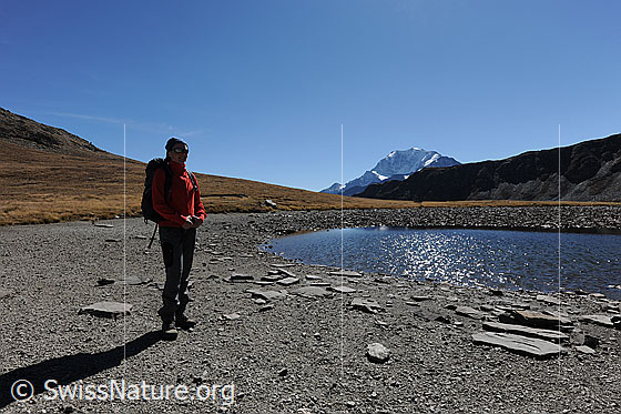 Foto: Wanderin an Bergsee (Undre Rossusee) mit Fletschhorn im Hintergrund. Der Wasserstand im See hat durch die Trockenheit abgenommen.