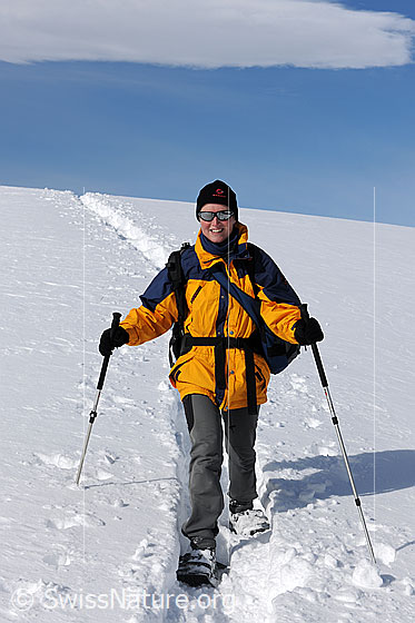 Foto: Schneeschuhläuferin auf Schneeschuhtour an einem sonnigen Wintertag. Am blauen Himmel ist ein Wolkenfeld zu sehen.