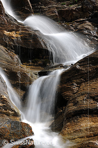 Foto: Kleine Wasserfälle über Felsbänder aus Bündner Schiefer. Langzeitbelichtung.
Hören Sie das erfrischende Rauschen des Wasserfalls?