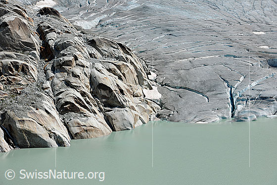 Foto: Rhonegletscher. Die Gletscherzunge mündet im Gletschersee. Im Fels ((Aaregranit) und Eis sind Strukturen zu sehen.
