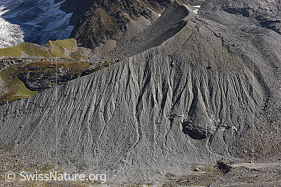 Foto: Seitenmoräne von Breithorngletscher und Grosshorngletscher. Der Breithorngletscher floss von rechts nach links, während der Grosshorngletscher von oben in den Breithorngletscher mündete. Dadurch enstand eine Seitenmoräne mit Kurve.
In der grünen Fläche links im Bild ist die Schmadrihütte zu sehen.
