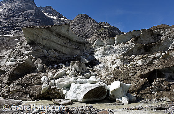 Foto: Unteraargletscher: Reste des Einsturztrichters von 2018/2019. Die südliche Begrenzung des Einsturztrichters zerfällt langsam. Relativ grosse Eisstücke haben sich aus der Eiswand gelöst und sind in den Gletscherbach gestürzt. Der grosse geschichtete Eisblock dürfte in der Zwischenzeit auch nicht mehr existieren.

