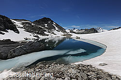 F119614: Felsblock und langezogene Eisscholle in Bergsee