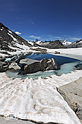 F119624: Felsblöcke in von Schnee umgebenem Bergsee